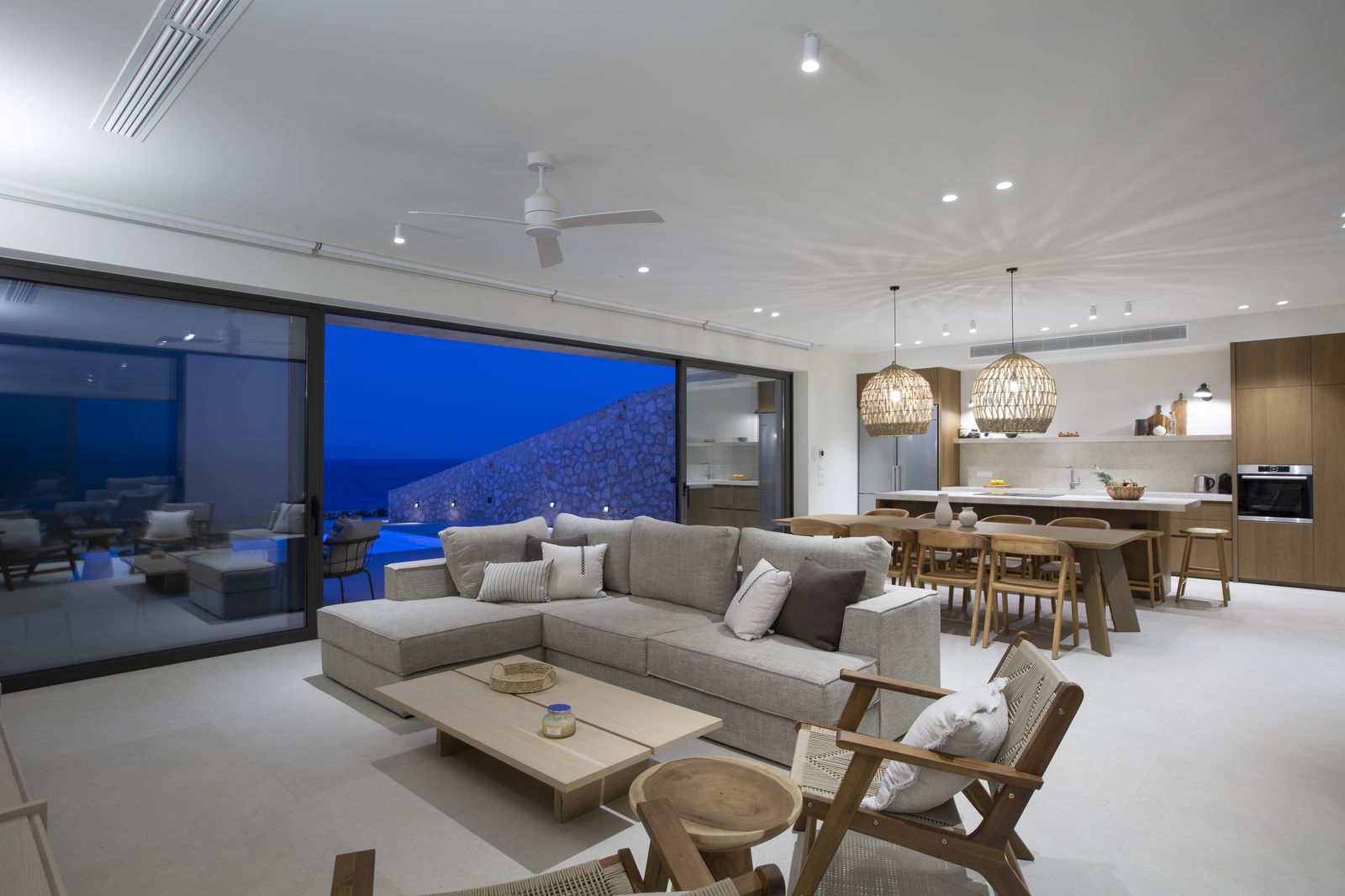 Open-plan living room at dusk with pool and sea view